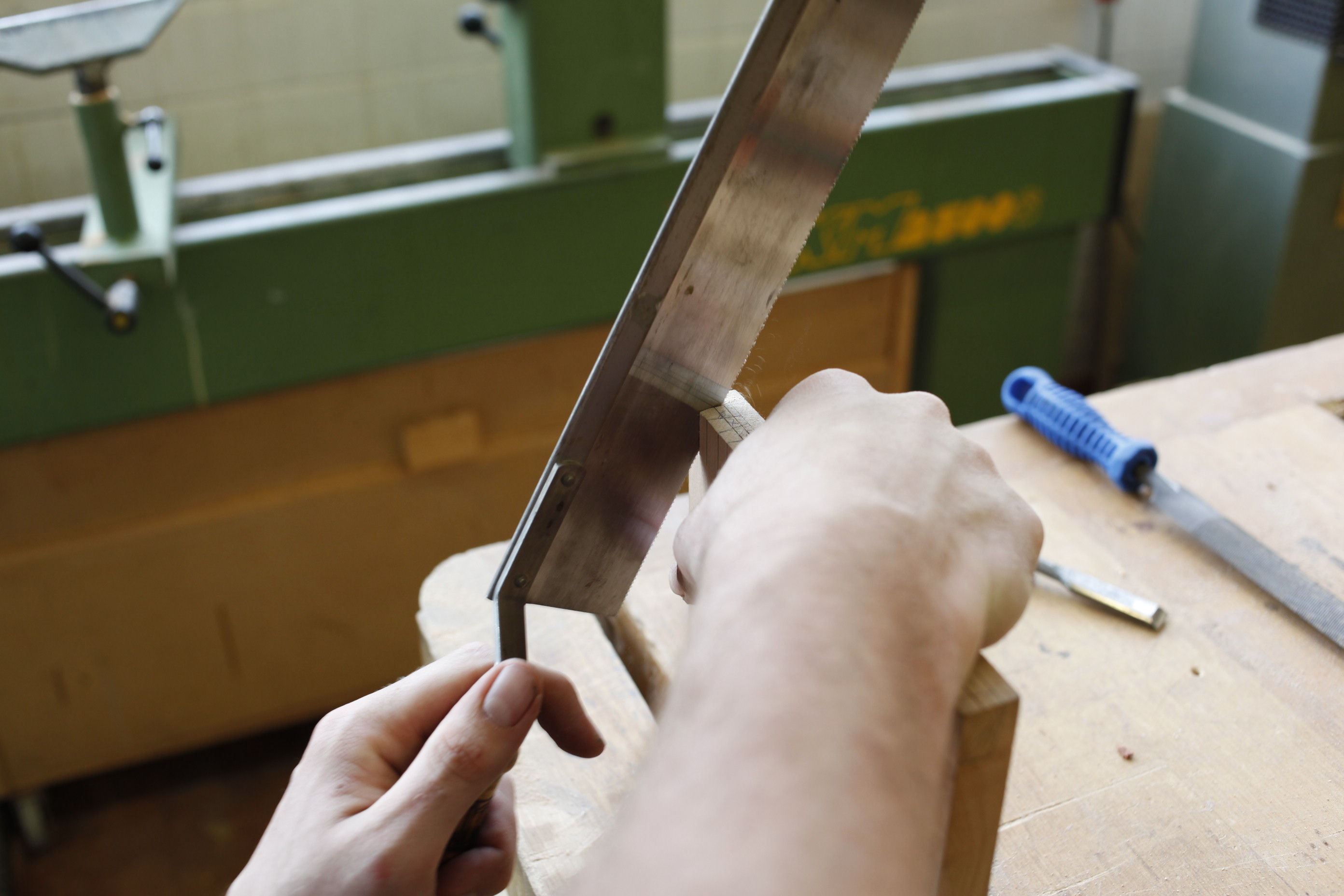 Person schneidet Holz mit einer Handsäge auf einer Werkbank in einer Holzwerkstatt.