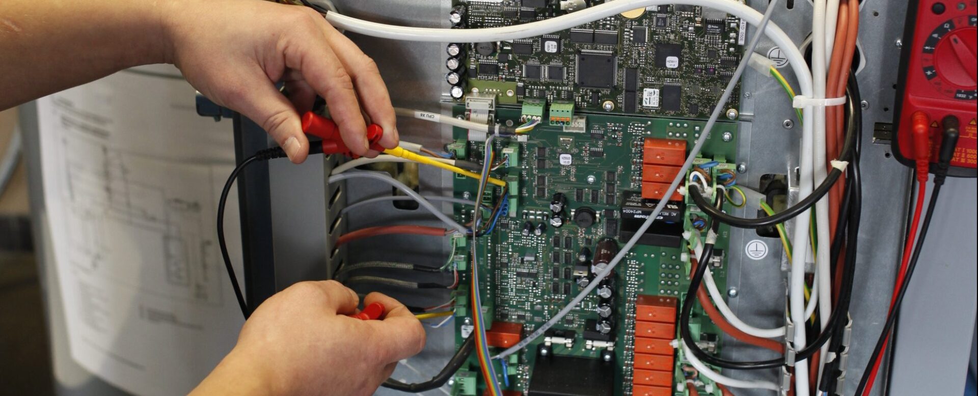 Techniker misst Spannung an einer offenen Schalttafel mit einem Multimeter, um die Elektronik zu überprüfen.