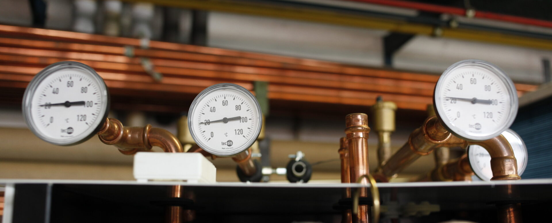 Mehrere Messgeräte auf Kupferrohren in einer industriellen Umgebung, zeigen Temperaturen bis 120°C.