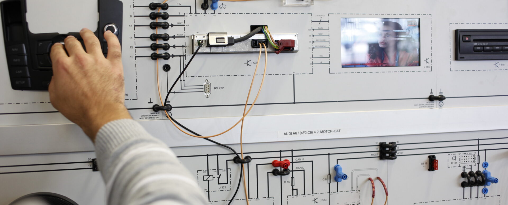 Person bedient ein elektronisches Testpanel mit Schaltplänen, Drähten und Tasten.