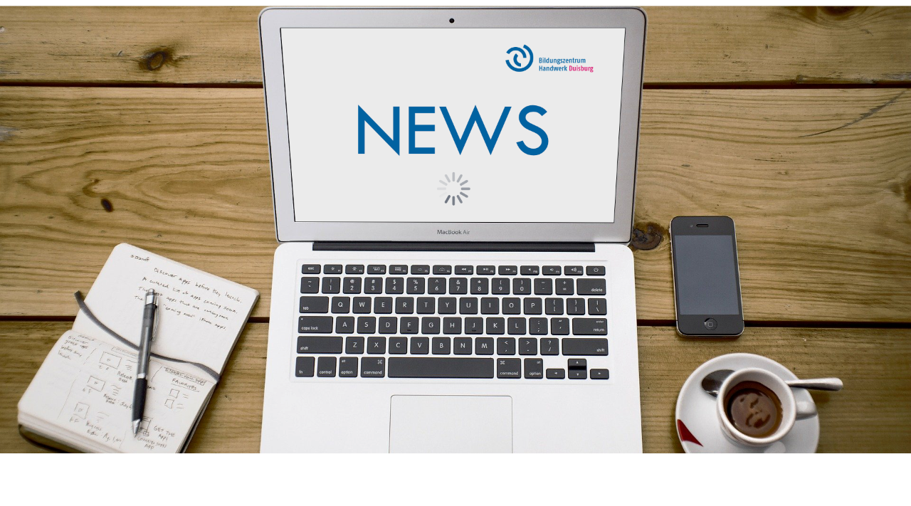 Laptop zeigt NEWS mit Ladeanzeige auf Holztisch, daneben ein Notizbuch mit Stift, Smartphone und eine Tasse Kaffee.