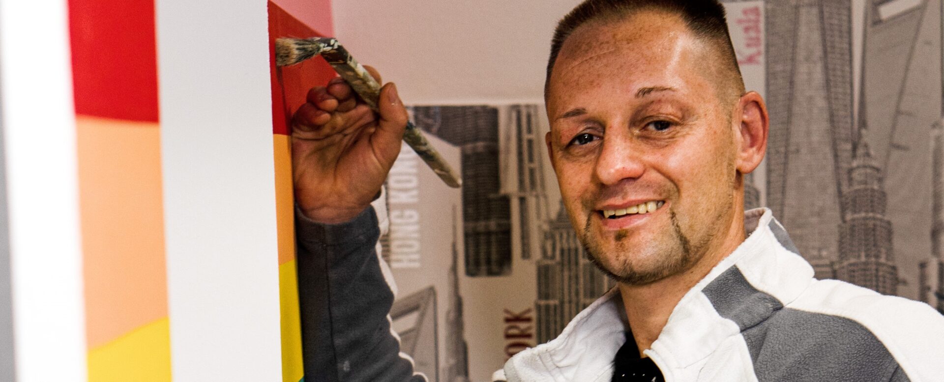 Mann malt Regenbogenstreifen an die Wand und lächelt
